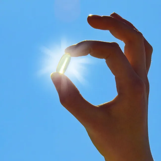 Woman holding vitamin up to sunlight for health benefits.